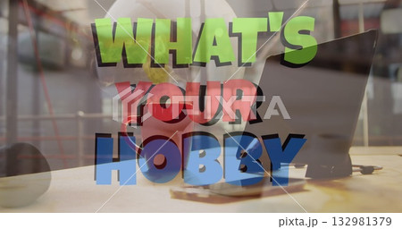 WHAT'S YOUR HOBBY text floating over desk in studio, with laptop, coffee mug, smartphone, lens cap 132981379