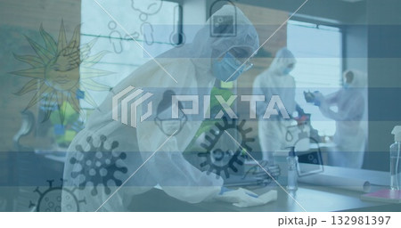 Cleaning technician in white coverall wiping desk at office workspace, with spray bottle and cloth 132981397