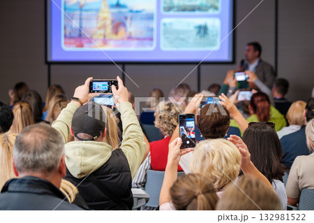 Audience at conference watches presentation and records with mobile phones and cameras 132981522