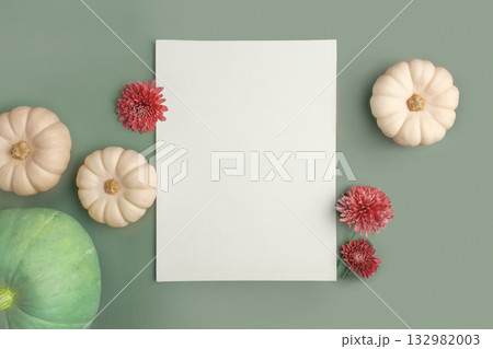 Blank paper sheet with decorations on pastel green background. Greeting card, invitation mockup. Place for inscription. Pumpkin, autumn flower. Modern Minimal business mock up, template. Top view note 132982003