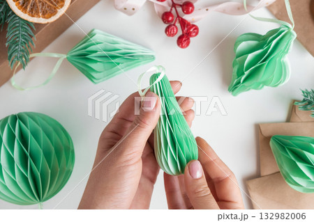 Female hands unfold paper Christmas honeycomb ornaments. Handmade foldable plastic free decor. Concept of winter creativity crafts. Trendy eco DIY. Scandinavian Modern decoration, minimalist. Top view 132982006