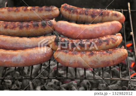 Grilled sausages. Cook man preparing grilling food bbq. Barbecue with smoke, flame outdoors. Tasty juicy german bratwurst. Charcoal kettle grill outside in backyard. Family summer vacation. Close-up Grilled sausages. Cook man preparing grilling food bbq. Barbecue with smoke, flame outdoors. Tasty juicy german bratwurst. Charcoal kettle grill outside in backyard. Family summer vacation. Close-up 132982012