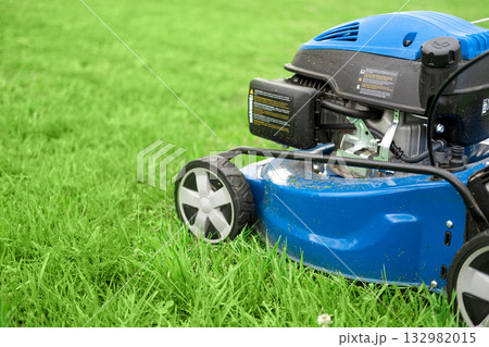 Lawn mower cutting grass. Small grass cuttings fly out of lawnmower. Grass clippings get spewed out of a mower pushed around by landscaper. CloseUp. Gardener working with mower machine. Mowing lawns 132982015