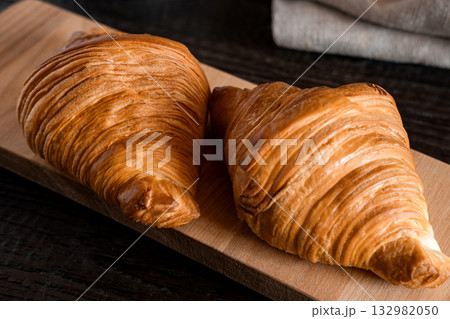 Two croissants on a wooden cutting board. Rustic dark table. Food series. Tasty fresh croissant, jam, orange juice. Continental breakfast served with freshly baked pastry. Close up view, Good morning 132982050