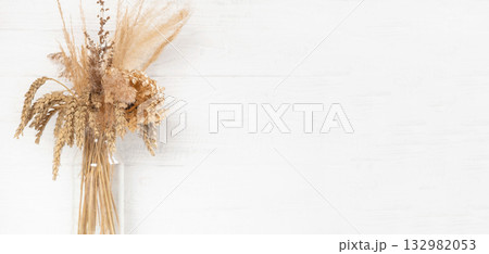 Beautiful decorative dried flowers, pampas grass, spikelets arrangement in a stylish transparent vase on white wooden rustic wall. Simple elegant home interior floral decor. Minimalistic composition Beautiful decorative dried flowers, pampas grass, spikelets arrangement in a stylish transparent vase on white wooden rustic wall. Simple elegant home interior floral decor. Minimalistic composition 132982053