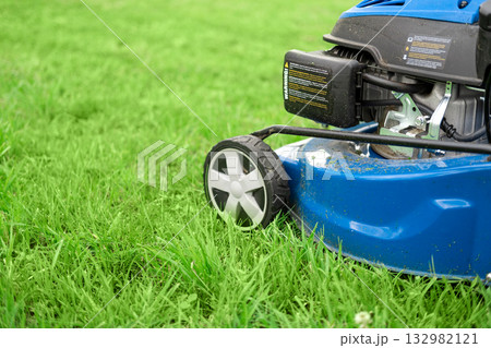 Lawn mower cutting grass. Small grass cuttings fly out of lawnmower. Grass clippings get spewed out of a mower pushed around by landscaper. CloseUp. Gardener working with mower machine. Mowing lawns Lawn mower cutting grass. Small grass cuttings fly out of lawnmower. Grass clippings get spewed out of a mower pushed around by landscaper. CloseUp. Gardener working with mower machine. Mowing lawns 132982121