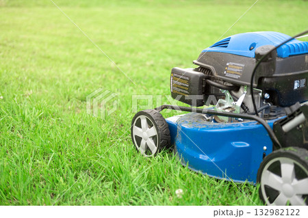 Lawn mower cutting grass. Small grass cuttings fly out of lawnmower. Grass clippings get spewed out of a mower pushed around by landscaper. CloseUp. Gardener working with mower machine. Mowing lawns Lawn mower cutting grass. Small grass cuttings fly out of lawnmower. Grass clippings get spewed out of a mower pushed around by landscaper. CloseUp. Gardener working with mower machine. Mowing lawns 132982122