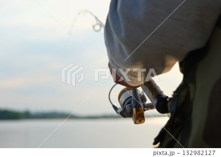 Old man fishing. Senior gray haired fisherman throws a spinning from shoreside at sunset, twisting a coil. Positive elderly male angling at lake, rotating reel rod. Retired fisher enjoying his weekend Old man fishing. Senior gray haired fisherman throws a spinning from shoreside at sunset, twisting a coil. Positive elderly male angling at lake, rotating reel rod. Retired fisher enjoying his weekend 132982127
