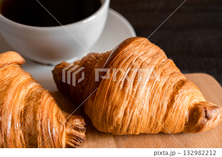 Coffee cup with croissant on a rustic dark wooden table. Food series. Two tasty fresh croissants, jam, orange juice. Continental breakfast served with freshly baked pastry. Close up view, Good morning Coffee cup with croissant on a rustic dark wooden table. Food series. Two tasty fresh croissants, jam, orange juice. Continental breakfast served with freshly baked pastry. Close up view, Good morning 132982212
