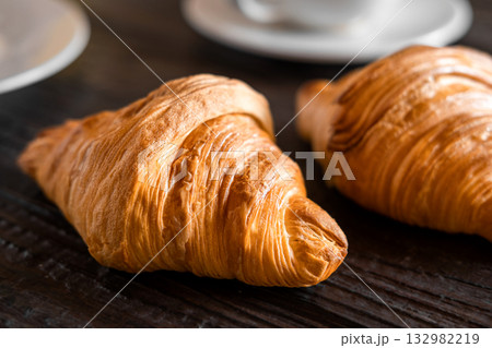 Coffee cup with croissant on a rustic dark wooden table. Food series. Two tasty fresh croissants, jam, orange juice. Continental breakfast served with freshly baked pastry. Close up view, Good morning Coffee cup with croissant on a rustic dark wooden table. Food series. Two tasty fresh croissants, jam, orange juice. Continental breakfast served with freshly baked pastry. Close up view, Good morning 132982219
