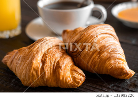 Coffee cup with croissant on a rustic dark wooden table. Food series. Two tasty fresh croissants, jam, orange juice. Continental breakfast served with freshly baked pastry. Close up view, Good morning Coffee cup with croissant on a rustic dark wooden table. Food series. Two tasty fresh croissants, jam, orange juice. Continental breakfast served with freshly baked pastry. Close up view, Good morning 132982220