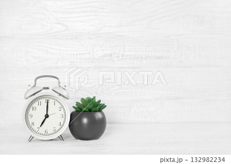 Front view white desk with alarm clock, houseplant and copy space. Morning background banner with free space for text. Minimalistic concept, workspace, time to work. Blank workplace. Office mock-up 132982234