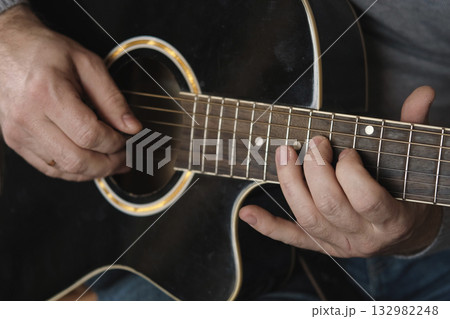Playing the guitar. Strumming acoustic guitar. Musician plays music. Man fingers holding mediator. Man hand playing guitar neck in dark room. Unrecognizable person rehearsing, fretboard close-up Playing the guitar. Strumming acoustic guitar. Musician plays music. Man fingers holding mediator. Man hand playing guitar neck in dark room. Unrecognizable person rehearsing, fretboard close-up 132982248