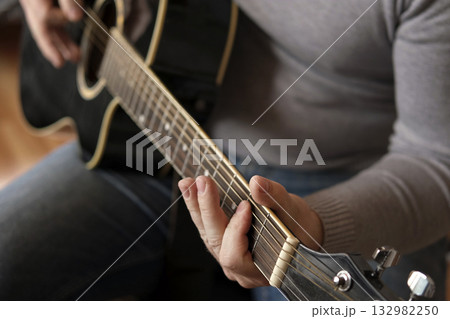 Playing the guitar. Strumming acoustic guitar. Musician plays music. Man fingers holding mediator. Man hand playing guitar neck in dark room. Unrecognizable person rehearsing, fretboard close-up Playing the guitar. Strumming acoustic guitar. Musician plays music. Man fingers holding mediator. Man hand playing guitar neck in dark room. Unrecognizable person rehearsing, fretboard close-up 132982250
