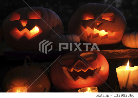 Halloween Pumpkin Head with Carved Scary Smiling Face at Night Outside. Jack-O-Lantern, Burning Candles Outdoor. Halloween Dark Composition Backyard Decor. Pumpkins Black Background. All Saints Day 4K 132982366