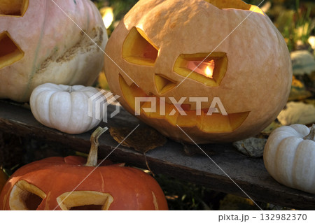 Halloween Pumpkin Head with Carved Scary Smiling Face on Wood Bench Outside. Jack-O-Lantern, Burning Candles, Dried Leaves Outdoors. Halloween Composition for Backyard Decor. Pumpkins. All Saints Day. Halloween Pumpkin Head with Carved Scary Smiling Face on Wood Bench Outside. Jack-O-Lantern, Burning Candles, Dried Leaves Outdoors. Halloween Composition for Backyard Decor. Pumpkins. All Saints Day. 132982370