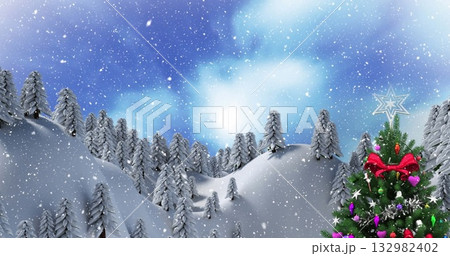 Standing Christmas tree topped with star under falling snow among evergreens in hills, copy space 132982402