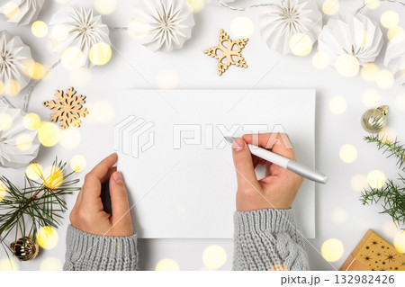 Woman Writing in Empty Notebook on White Desk. Girl Hands with Pen Among Gift Box and Winter Festive Decor. Diary, Holiday Greeting or Planning. Top view, Mock up. Paper Blank Sheet. Eco Nordic Design 132982426