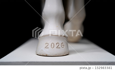 Ceramic horse hoof with engraved 2026 on a white pedestal; macro studio detail with strong contrast 132983381