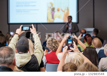 Audience at conference filming presenter on stage with smartphones during a professional event in front room 132983544
