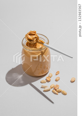 Peanut butter in glass jar on gray background with spoon and scattered salted nuts. 132983567