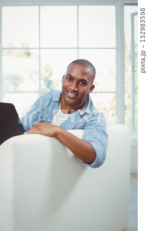 African American man wearing blue shirt, white t-shirt sitting on couch in living room using laptop African American man wearing blue shirt, white t-shirt sitting on couch in living room using laptop 132983598