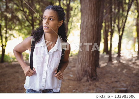 Middle-aged woman pausing on hiking trail in forest wearing white shirt with backpack, copy space 132983606
