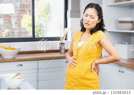 Korean pregnant woman in yellow maternity dress leaning on countertop in kitchen by fruit bowl Korean pregnant woman in yellow maternity dress leaning on countertop in kitchen by fruit bowl 132983613