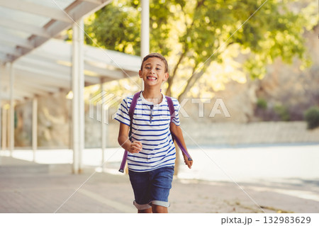 Male child running along paved walkway under white metal canopy carrying purple backpack 132983629