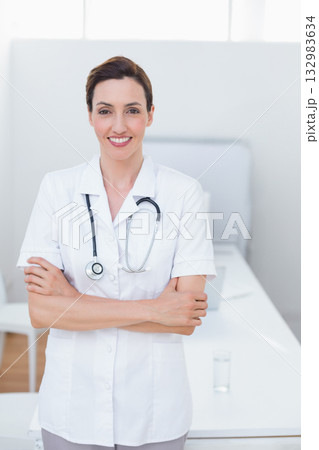 Middle aged female doctor wearing tunic and stethoscope standing in exam room by exam table 132983634