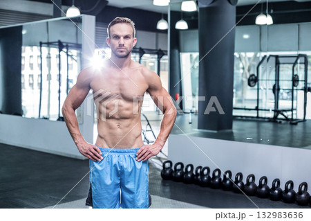 Adult male standing in gym wearing blue athletic shorts and showcasing kettlebells mirrored wall Adult male standing in gym wearing blue athletic shorts and showcasing kettlebells mirrored wall 132983636