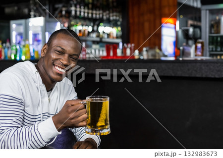 African American man wearing white hoodie sitting at pub counter holding clear beer mug, copy space 132983673
