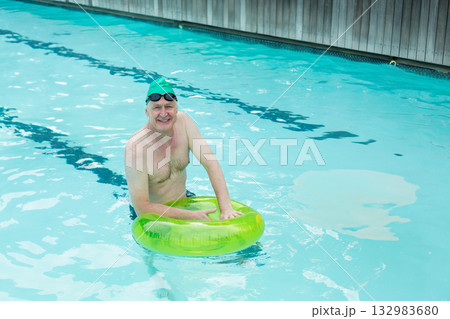 Senior white man wearing green swim cap and goggles floating in pool lanes holding lime-green ring Senior white man wearing green swim cap and goggles floating in pool lanes holding lime-green ring 132983680