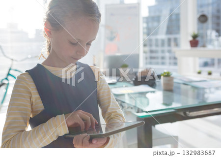 Female child tapping on tablet in office beside bicycle frame and conference table with succulents 132983687