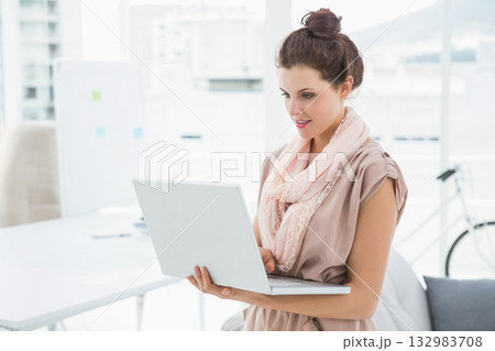 Woman standing holding laptop in workspace near whiteboard with sticky notes and bicycle by desk 132983708