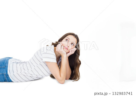 Woman lying on stomach on white backdrop wearing striped top and jeans propping chin looking upward Woman lying on stomach on white backdrop wearing striped top and jeans propping chin looking upward 132983741