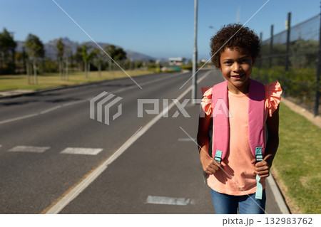 African American girl holding pink backpack on sidewalk beside road pavement markings, copy space African American girl holding pink backpack on sidewalk beside road pavement markings, copy space 132983762