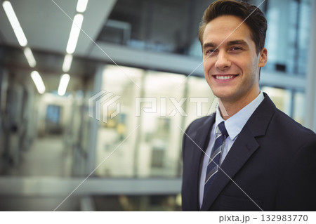 Man standing in office hallway wearing suit jacket and striped tie under linear lights, copy space 132983770