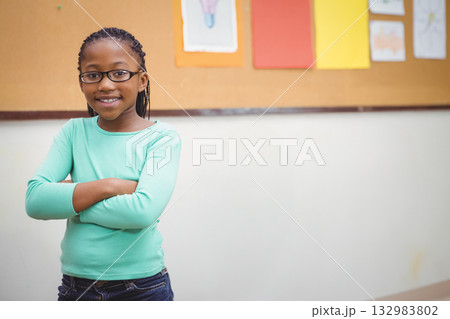 African American child standing and smiling in classroom by cork board with drawings, copy space African American child standing and smiling in classroom by cork board with drawings, copy space 132983802