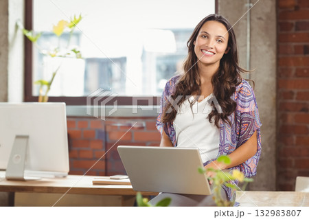 Woman in cardigan holding laptop while sitting at desk with plants in office space, copy space 132983807