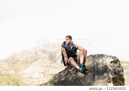 Male hiker sitting on boulder on rocky hillside wearing hiking backpack and trail shoes and smiling 132983828