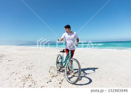 Man pushing teal bicycle along white sand beach under clear blue sky with turquoise ocean horizon Man pushing teal bicycle along white sand beach under clear blue sky with turquoise ocean horizon 132983846