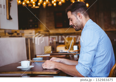 Man sitting at wooden table in coffee shop wearing striped shirt holding white cup, copy space 132983875
