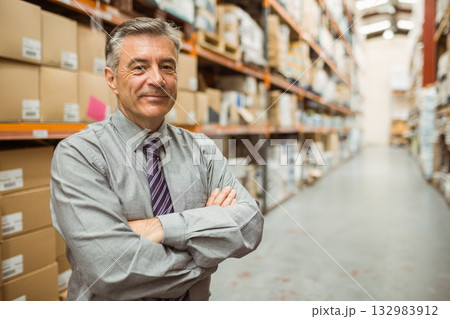 Middle-aged man standing in warehouse wearing business attire with boxes under fluorescent lights 132983912