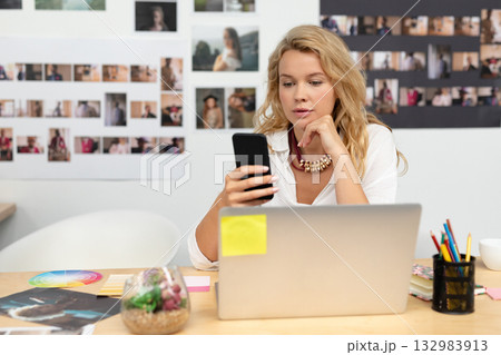 Woman sitting at wooden desk in creative studio using laptop with color wheel, sticky notes nearby Woman sitting at wooden desk in creative studio using laptop with color wheel, sticky notes nearby 132983913