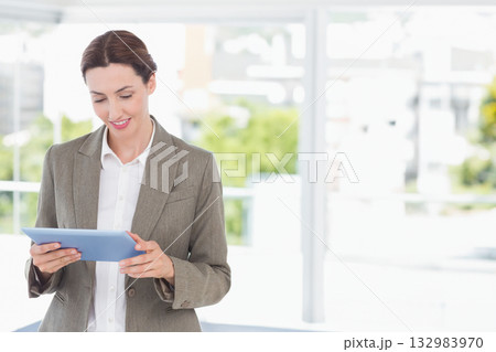 Blazer-clad woman holding blue tablet near office glass wall with white window railing, copy space 132983970