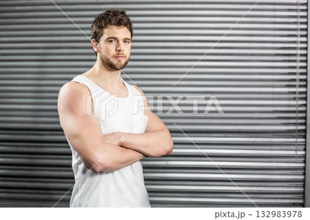 Muscular man posing with arms crossed in garage beside corrugated roller shutter door, copy space 132983978