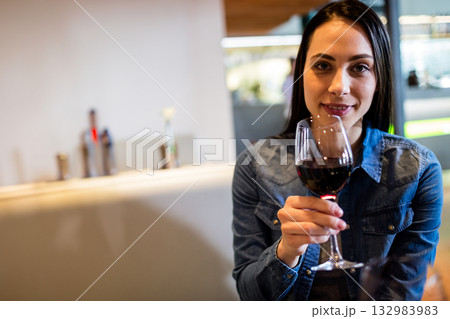 Woman sitting at bar counter holding wine glass with red wine under warm lighting, copy space Woman sitting at bar counter holding wine glass with red wine under warm lighting, copy space 132983983