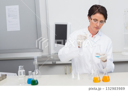 Female scientist pouring blue solution from flask into funnel with pipette at lab bench, copy space 132983989