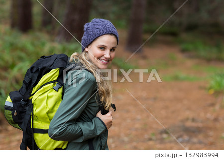 Female hiker in purple beanie green jacket walking on trail with hiking backpack glancing back Female hiker in purple beanie green jacket walking on trail with hiking backpack glancing back 132983994